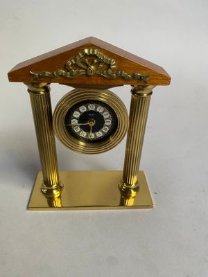 une petite horloge dorée avec un cadran noir, posée sur un socle