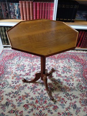 une table octogonale avec un plateau en bois, posée sur un tapis devant une bibliothèque
