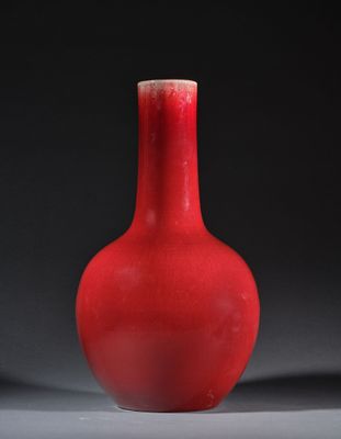 un vase rouge posé sur une surface grise, sur fond noir