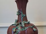 un vase rouge orné de feuilles vertes, posé par terre