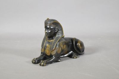 une statue en bronze représentant un sphinx assis sur une surface blanche