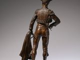 bronze statue of a man with a cape and a bag