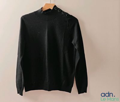 un pull noir suspendu à un cintre contre un mur