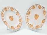 two plates with orange flowers on them sitting on a stand