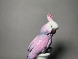 a figurine of a pink cockatoo sitting on top of a white vase