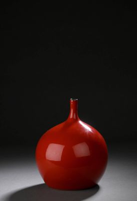 un vase rouge posé sur une table près d'un mur noir