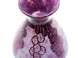 a purple vase with grapes on it on a white surface