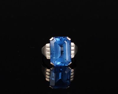une bague en topaze bleue et diamants posée sur un fond noir
