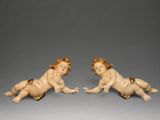deux figurines représentant des bébés couchés sur le ventre sur une surface grise