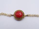 a close up of a bracelet with pearls and a red stone