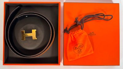 une boîte orange ornée d'une ceinture noire et d'un logo « h » doré