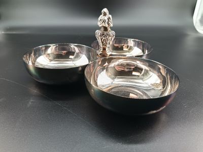 two silver dishes sitting on a table with a figurine on top of them