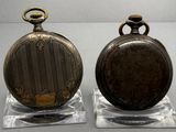 two antique pocket watches sitting on display on a table