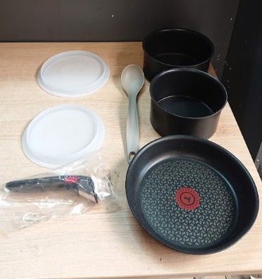 plusieurs casseroles et poêles posées sur une table, avec un couteau et une cuillère