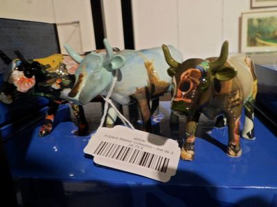 trois figurines de vaches posées sur une table bleue, avec une étiquette de prix