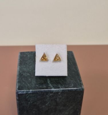 une paire de boucles d'oreilles en forme de triangle en or posées sur un bloc de marbre
