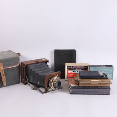 un vieil appareil photo, un livre, un étui à appareil photo et d'autres objets sont posés sur une surface blanche