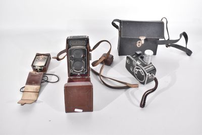trois vieux appareils photo et un portefeuille posés sur une surface blanche