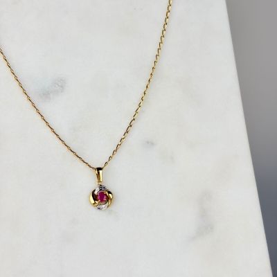 un collier plaqué or orné d'un pendentif en pierre rose posé sur un fond en marbre blanc