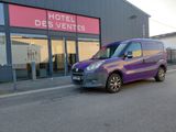 une camionnette violette garée devant un immeuble sur lequel est accrochée une enseigne indiquant « Hôtel des ventes »