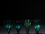 four green wine glasses are lined up in a row on a table