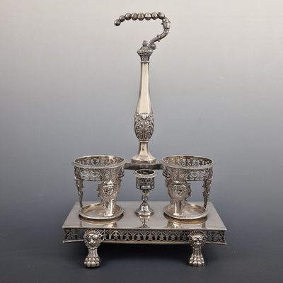 un plateau en argent avec trois tasses et un vase posé sur un socle