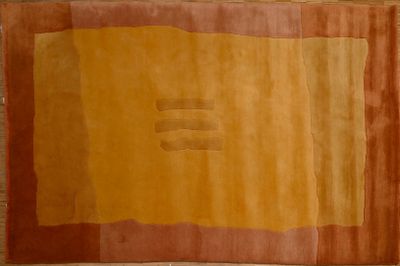 an orange and yellow rug on a wooden floor with a brick wall in the background
