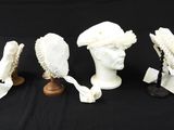 trois têtes de mannequins blanches coiffées de chapeaux, sur fond noir
