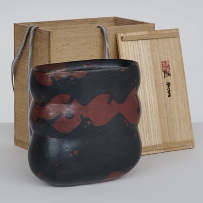 un vase noir et rouge posé à côté d'une boîte en bois