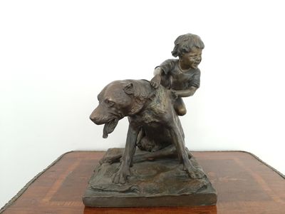 une statue en bronze représentant un garçon et un chien, posée sur une table
