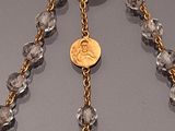 rosary chain with gold coin and crystal beads on a gray surface