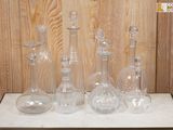 cinq vases en verre posés sur une table devant un mur lambrissé