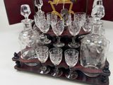 bottles and glasses are arranged on a wooden stand with a clock in the background