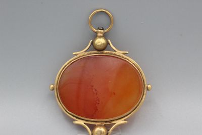 une image représentant un pendentif en pierre dorée et rouge sur fond blanc