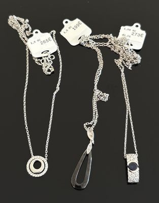 trois colliers en argent ornés d'étiquettes, posés sur un fond noir