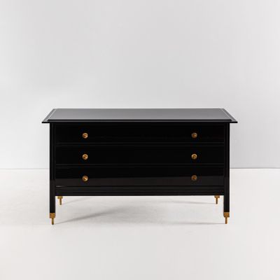 une commode noire avec des poignées en laiton et un plateau noir