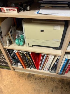 a printer sitting on top of a book shelf in front of a television