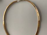 a gold necklace on a white table next to a pair of scissors