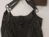 black purse with tassels hanging from it on a bed