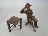 a bronze statue of a man sitting on a chair next to a stool