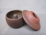 un petit pot marron avec un couvercle, posé sur une surface blanche