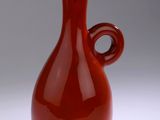 un vase rouge posé sur une surface blanche