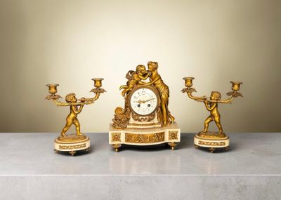 une horloge en or posée sur une table, à côté de trois bougies