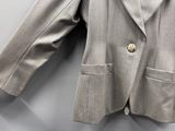 une veste grise boutonnée, suspendue à un cintre sur un mur blanc