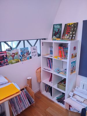 une pièce avec un bureau, une bibliothèque et des photos accrochées au mur