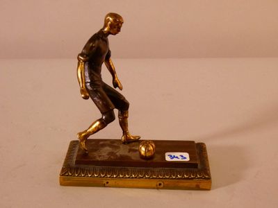 figurine en bronze représentant un footballeur avec un ballon, posée sur une balance