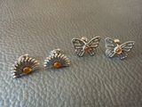 trois boucles d'oreilles en forme de papillon, argentées et orange, posées sur un fond en cuir