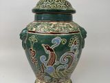 un vase vert orné d'un oiseau sur fond blanc