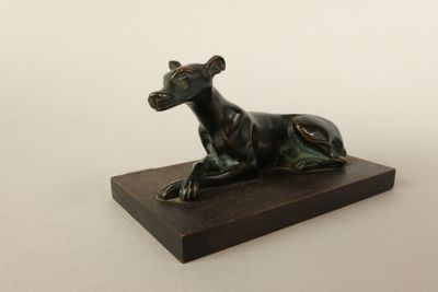 sculpture en bronze représentant un chien, posée sur un socle en bois, sur fond blanc