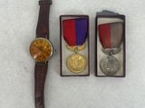 three medals and a watch sitting on top of a white surface